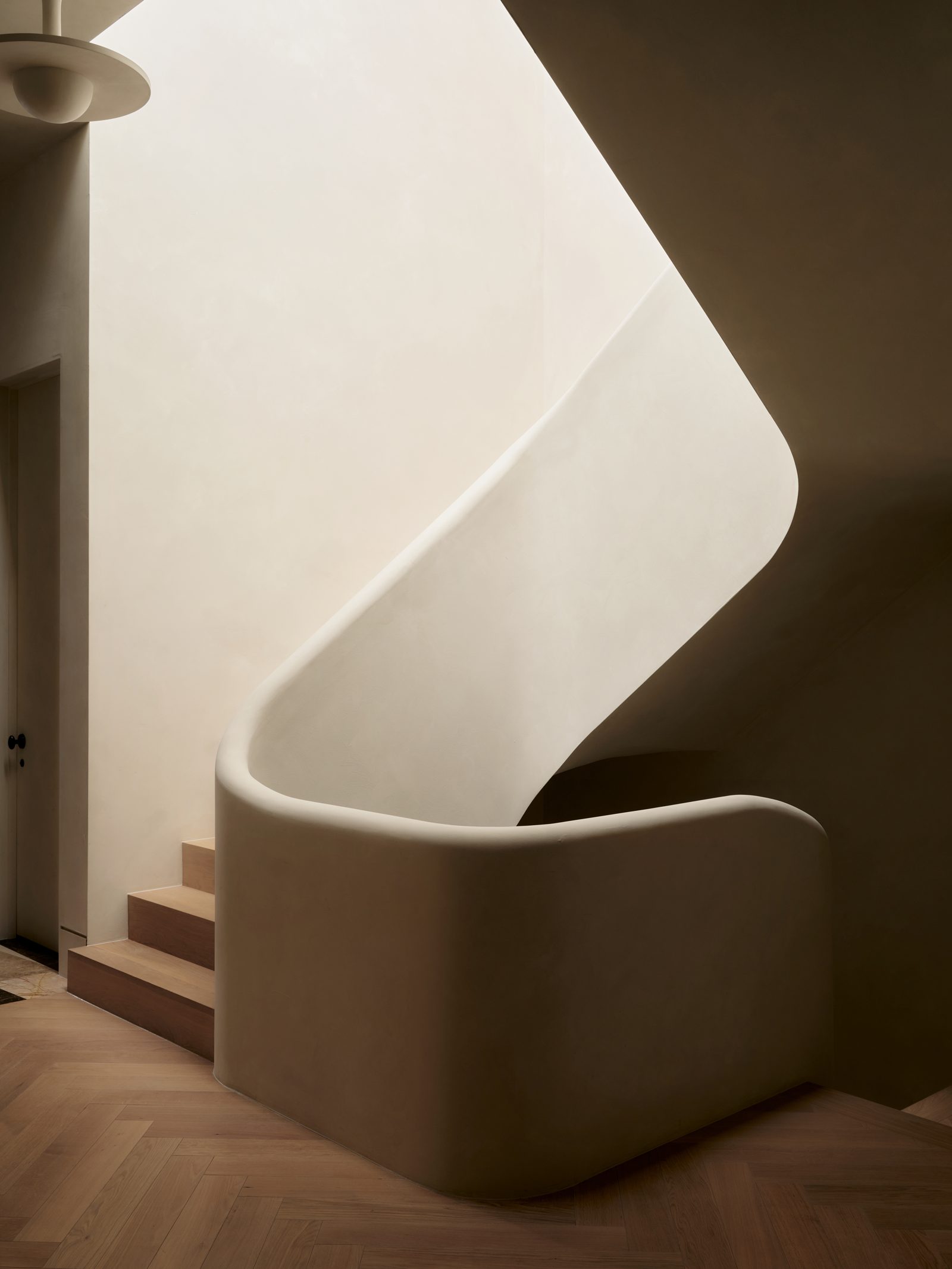 A curved plaster stair, its handrail one continuous ribbon of plaster, over a herringbone oak floor